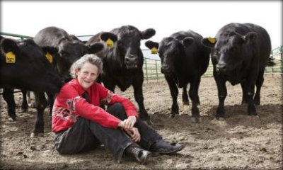 Immagine: foto di Temple Grandin seduta a terra davanti e dietro di lei 4 mucche nere