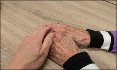 Immagine: una mano di persona giovane tiene le mani di una persona anziana, appoggiate su un tavolo