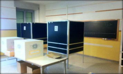 Immagine: foto di una tipica aula per seggio elettorale. In una classe di scuola, grandi scatole di raccolta sopra ai banchi