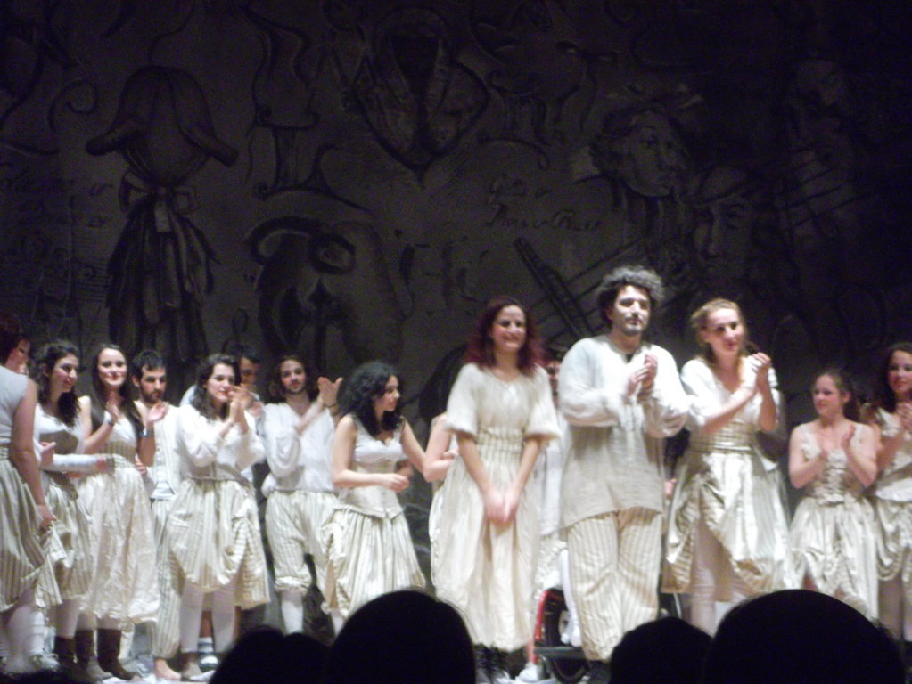 Foto spettacolo teatrale serale con attori in bianco al momento degli applausi