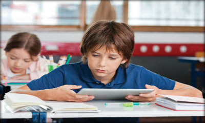 Immagine: foto primopiano di un bambino sul banco di scuola che legge sul tablet