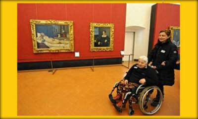 Immagine: foto di persona che spinge una signora anziana su carrozzina dentro un museo