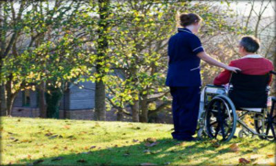 Immagine: Una persona con disabilità motoria, assieme alla sua assistente, su un prato, al sole.